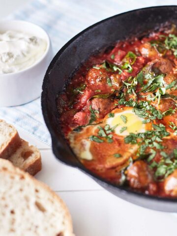 Baked meatballs in tomato sauces with eggs, topped with parsley in a cast iron skillet, with a side of crusty bread