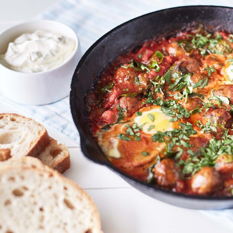 Baked meatballs in tomato sauces with eggs, topped with parsley in a cast iron skillet, with a side of crusty bread