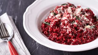 Vibrant red risotto, dusted with parmesan cheese in a white bowl on a black background