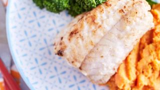 Pan fried white fish on mashed sweet potato with and broccolini with patterned plate on baby fox printed table cloth with red utensils