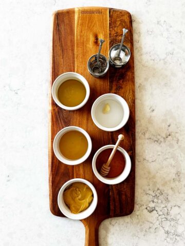 Measured ingredients for Dijon dressing on wooden board with mustard, vinegar, garlic and oil