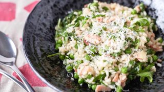 Risotto with vibrant green peas, bacon, rocket leaves and shaved parmesan in a black bowl