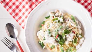 Spaghetti with fresh herbs, fish, beans and specks of chilli on a white plate with red utensils or chequered red and white table cloth