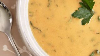 Yellow creamy soup topped with herbs in a bowl