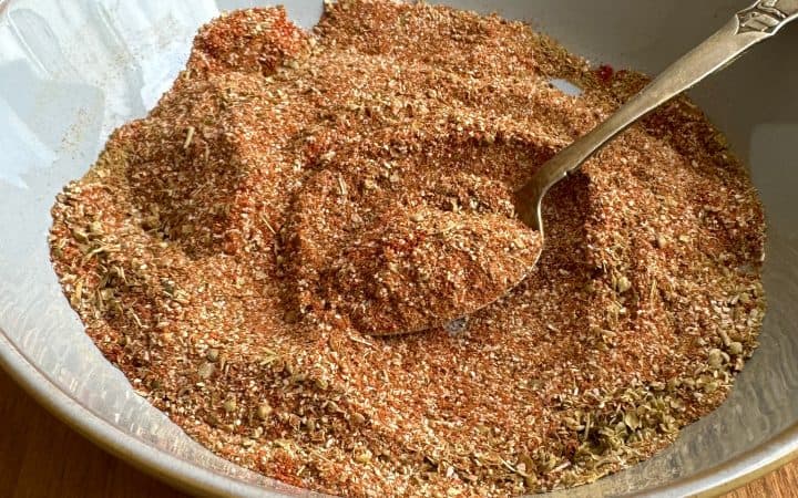 Blend of spices in a light blue bowl with an antique spoon on a wooden table