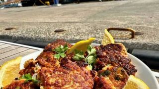 Delicious leftover fish cakes, with lemon wedge on plate with fishing trawlers in background