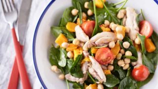 Vibrant bowl of roasted pumpkin salad featuring chicken, sliced cherry tomatoes, chickpeas, and roasted pumpkin, all served on a bed of fresh spinach.