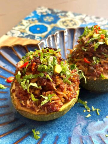 Two round zucchini dolmas stuffed with a rice and mince mixture, topped with fresh herbs, served on a blue plate.