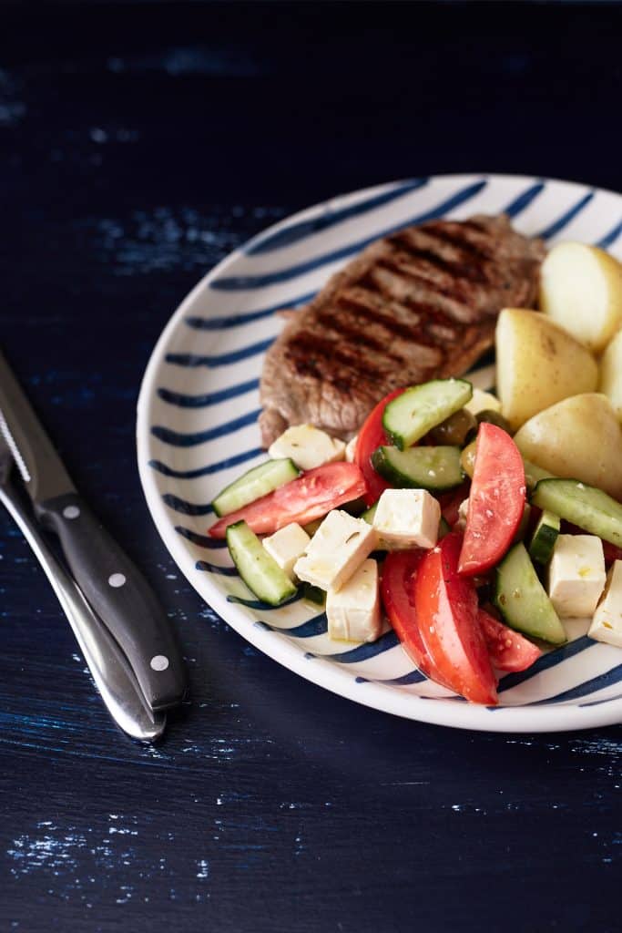 Grilled Rump Steak with new potatoes and greek salad on a plate.