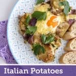 A patterned plate holds sliced baked potatoes with red onion and chorizo, topped by a cheesy baked egg and garnished with parsley, served alongside crusty bread.