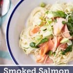 White plate with delicate angel hair pasta topped with slices of smoked salmon, cubed avocado, fresh watercress, and thinly sliced spring onions.