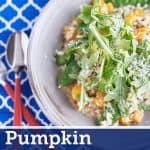 A creamy sage risotto with cubed pumpkin and snow peas, topped with rocket leaves, Parmesan cheese, and lemon zest, served on a light grey plate on a patterned blue tablecloth.