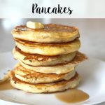 Six fluffy protein buttermilk pancakes stacked on top of each other with melting butter and drizzled maple syrup on a white plate.