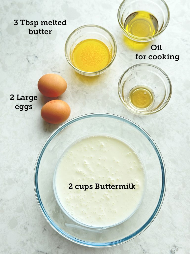 All the wet ingredients for the protein buttermilk pancakes are measured and in separate containers laid out on a marble surface.