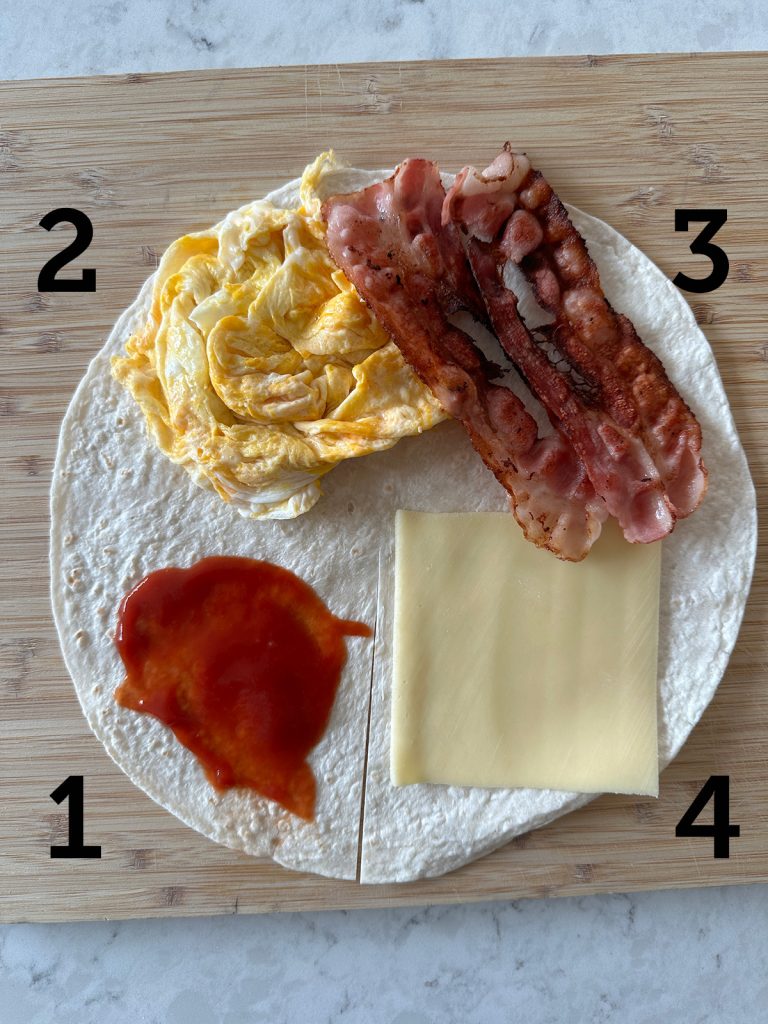 A wrap divided into four quarters with one cut from the center to the edge: sauce in the first, scrambled eggs in the second, two pieces of bacon in the third, and a slice of cheese in the fourth.