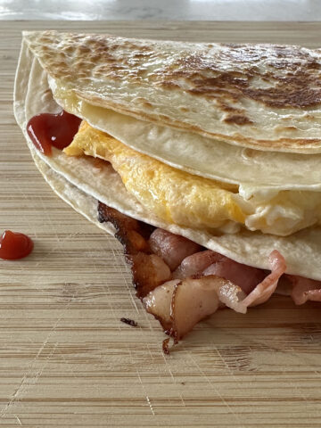 Bacon, egg, and cheese folded into a wrap with a nicely fried top on a wooden cutting board.