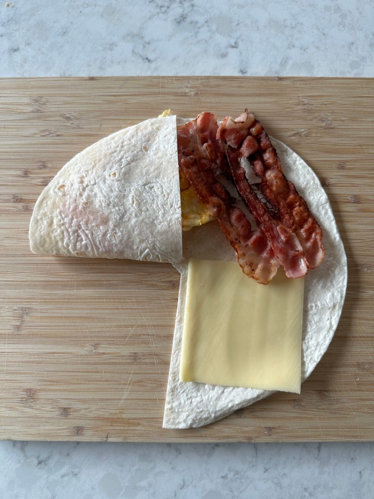 A wrap folded with bacon and cheese on wooden cutting board