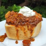 South African bunny chow, a hollowed-out ¼ loaf of bread filled with beef curry, topped with a dollop of yogurt and cilantro.