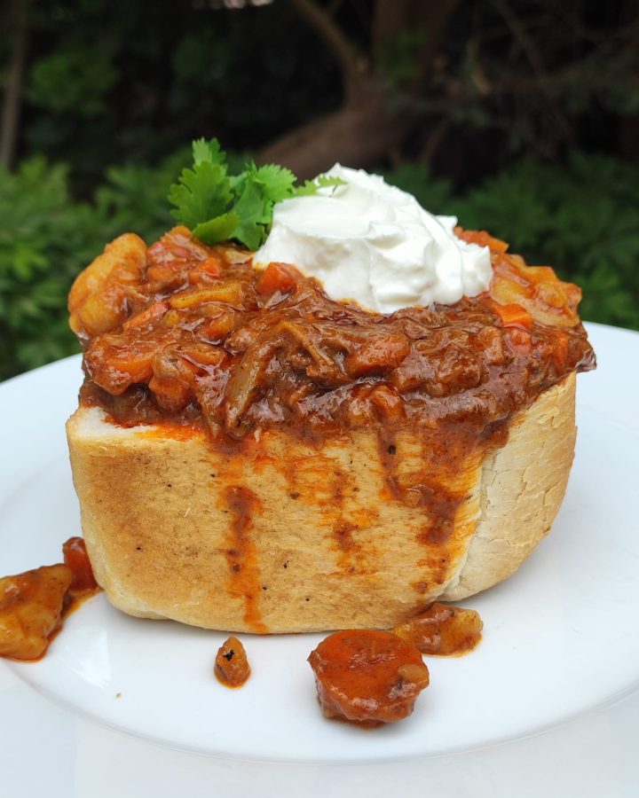 South African bunny chow, a hollowed-out ¼ loaf of bread filled with beef curry, topped with a dollop of yogurt and cilantro.