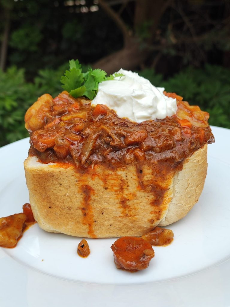 South African bunny chow, a hollowed-out ¼ loaf of bread filled with beef curry, topped with a dollop of yogurt and cilantro.