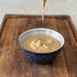 Tandoori mayonnaise in a blue bowl on a wooden board with mayonnaise dripping from a spoon into the bowl