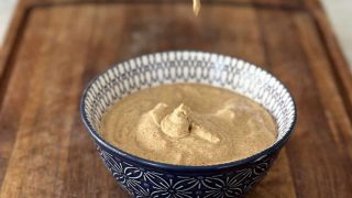 Tandoori mayonnaise in a blue bowl on a wooden board with mayonnaise dripping from a spoon into the bowl