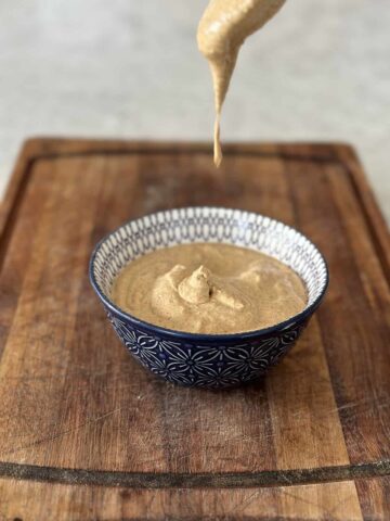 Tandoori mayonnaise in a blue bowl on a wooden board with mayonnaise dripping from a spoon into the bowl