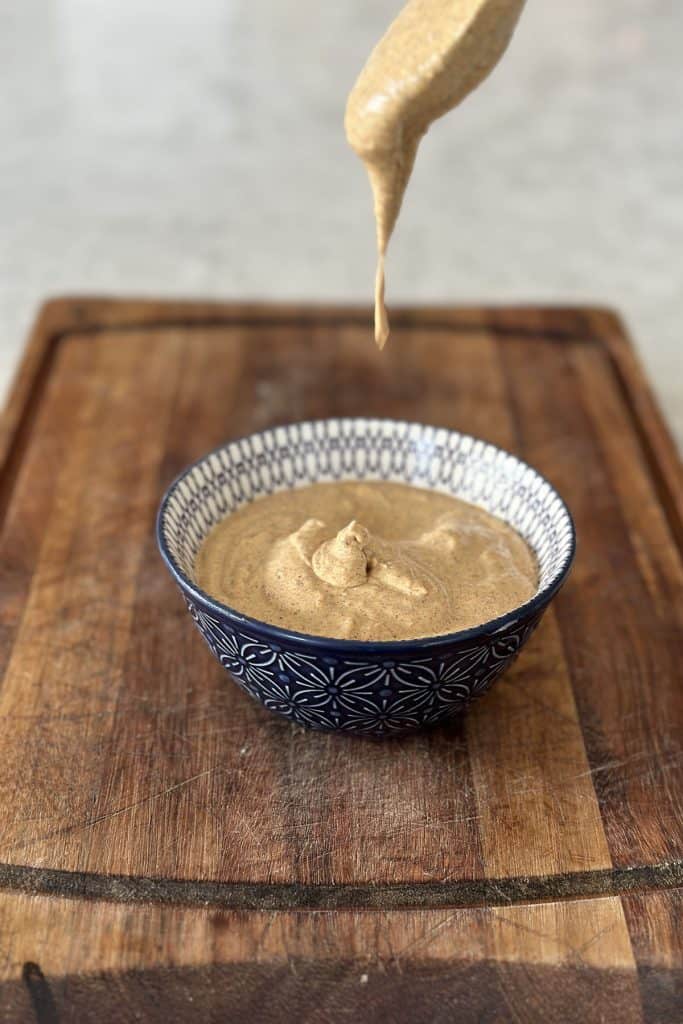 Tandoori mayonnaise in a blue bowl on a wooden board with mayonnaise dripping from a spoon into the bowl