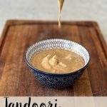 Tandoori mayonnaise in a blue bowl on a wooden board with mayonnaise dripping from a spoon into the bowl