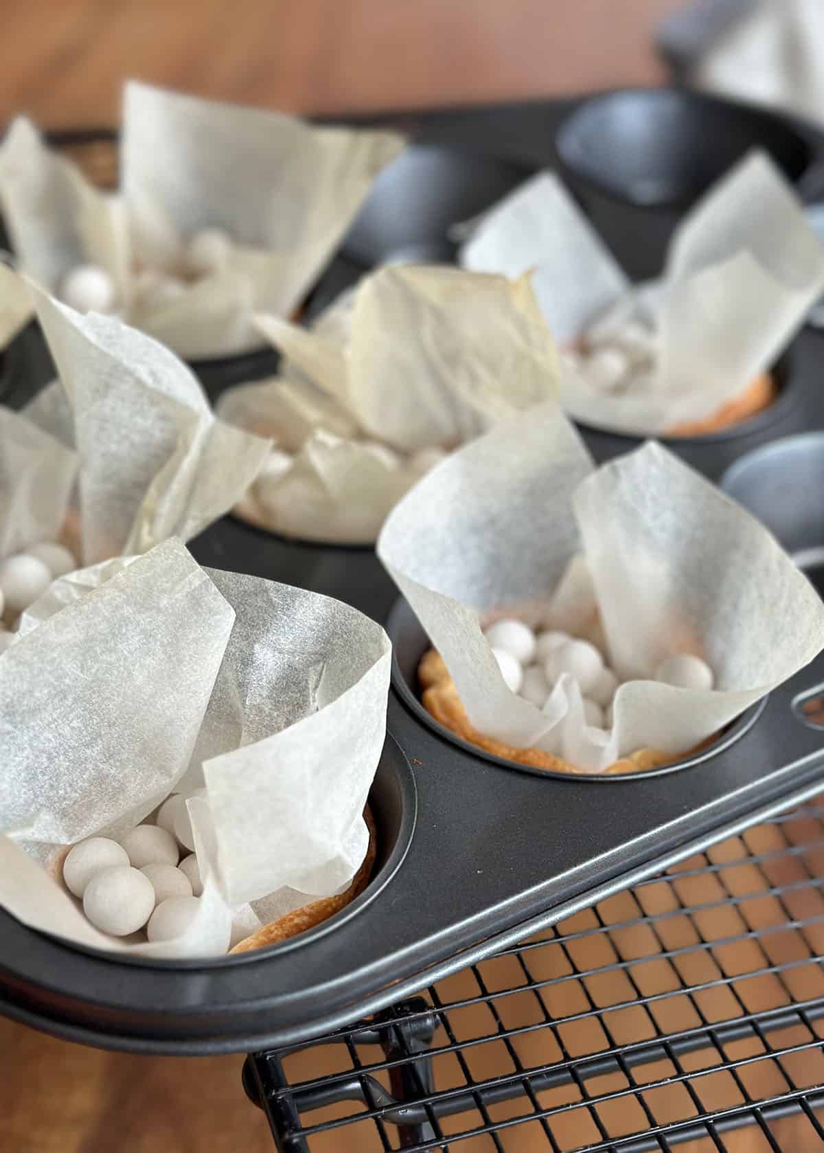 Baked pastry cases in a muffin tin, still containing weights.