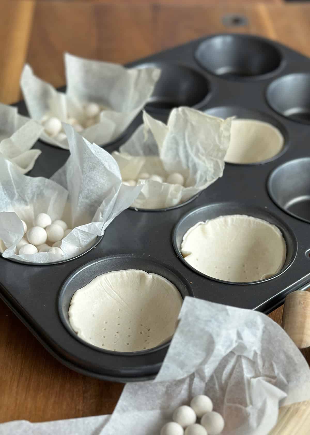 Muffin tin filled with puff pastry, each cup topped with a square of baking paper and weights.