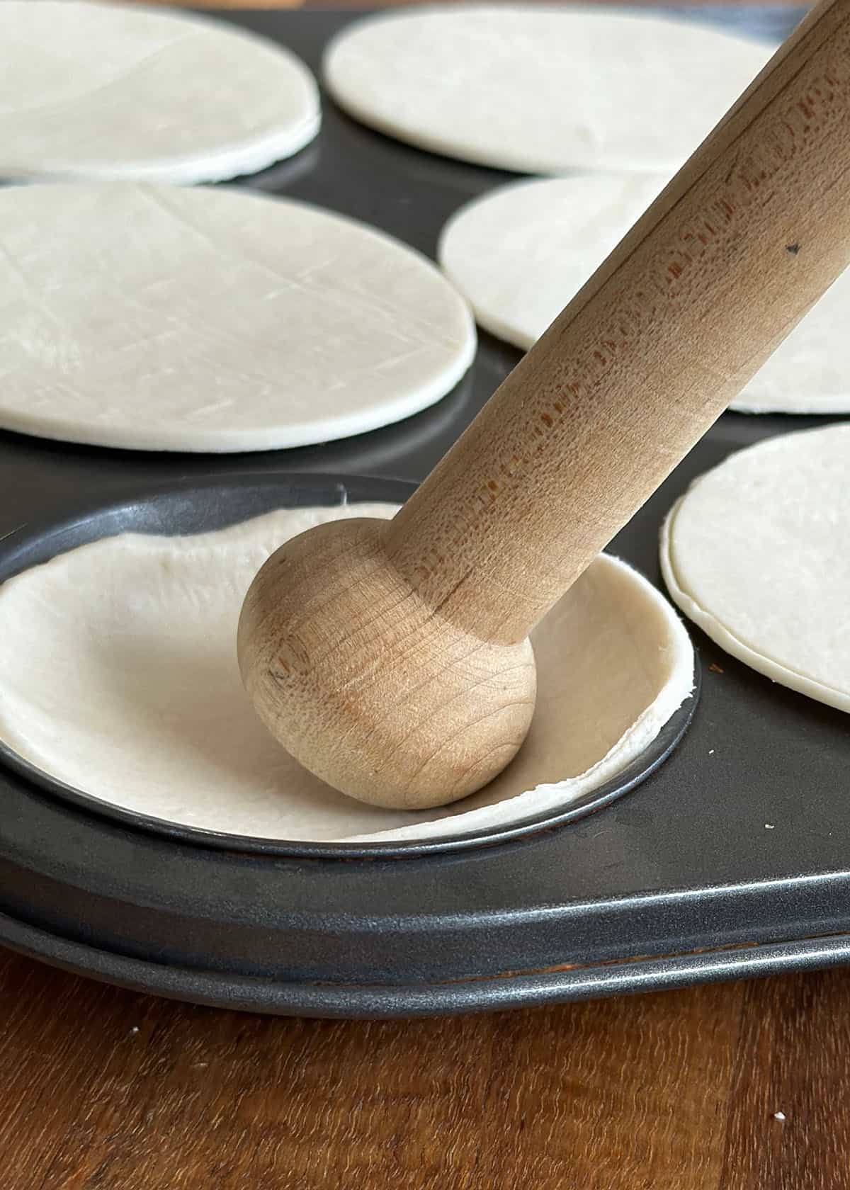 A wooden pastry press is used to gently press round cuts of puff pastry into the muffin tin cups, ready to bake the cases for Nutella tartlets.