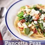 A white bowl with blue rim filled with pasta with pancetta and peas, topped with torn basil leaves, spinach, cherry tomatoes, and crumbled feta.