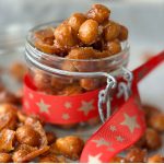 Honey roasted macadamia nuts spread on a cookie sheet and inside a glass mason jar decorated with a Christmas ribbon.