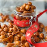 Honey roasted macadamia nuts spread on a cookie sheet and inside a glass mason jar decorated with a Christmas ribbon.