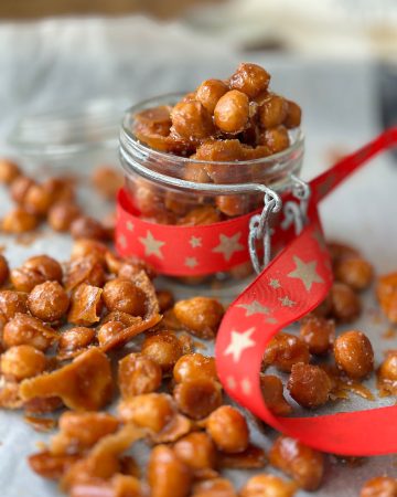 Honey roasted macadamia nuts spread on a cookie sheet and inside a glass mason jar decorated with a Christmas ribbon.