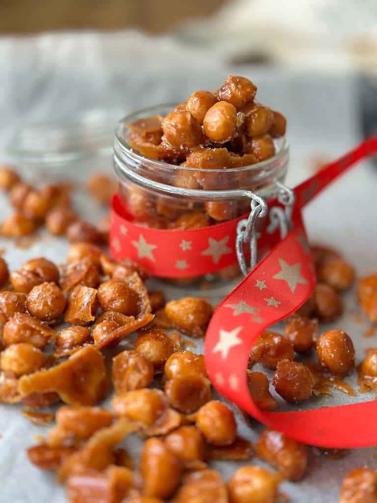 Honey roasted macadamia nuts spread on a cookie sheet and inside a glass mason jar decorated with a Christmas ribbon.