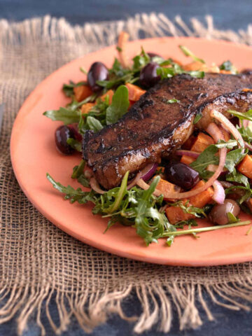 Juicy steak on arugula salad with roasted sweet potato, olives and red onion