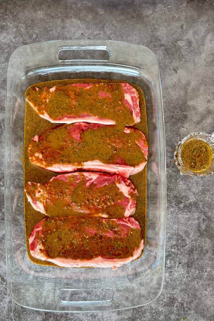 Porterhouse steaks marinating in glass bowl for arugula and steak salad.