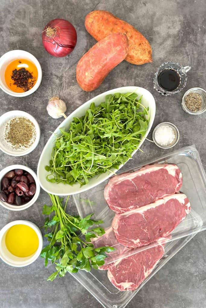 Ingredients for Arugula salad with steak arranged on kitchen bench with fresh produce.