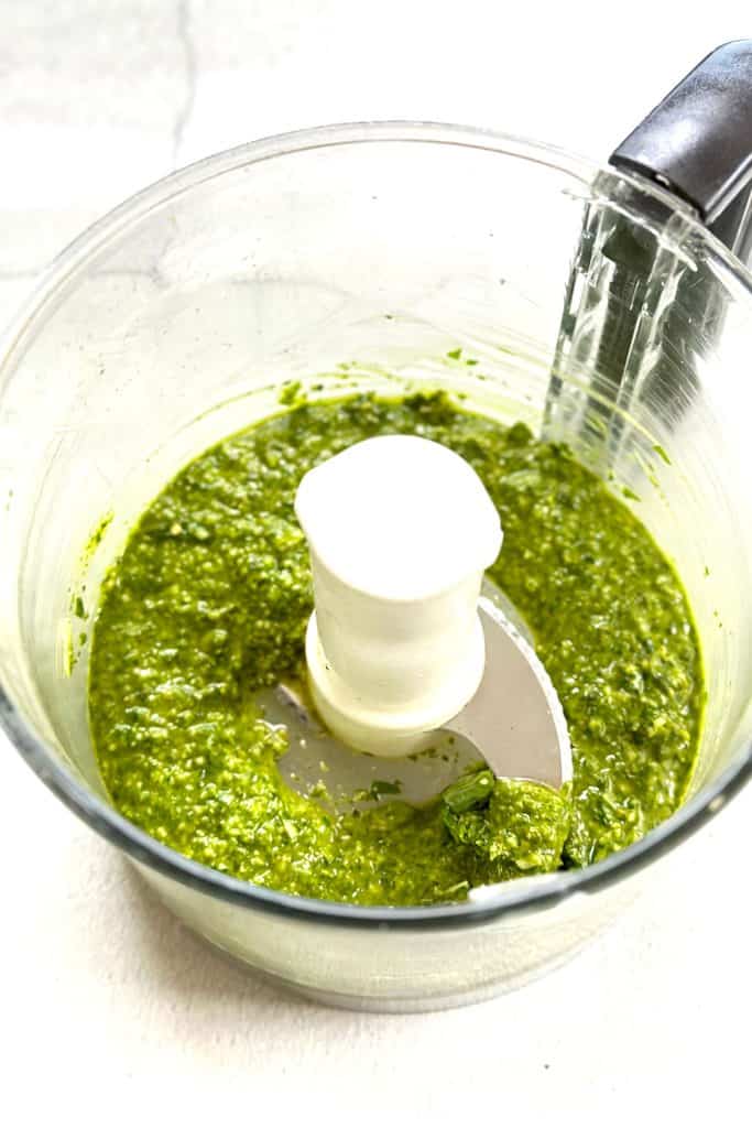 Smooth yet chunky basil pesto in a food processor on a white marble table top