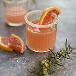 Two sugar-rimmed glasses filled with pink grapefruit gin cocktails, garnished with fresh rosemary sprigs and slices of grapefruit.