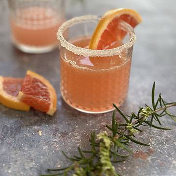 Two sugar-rimmed glasses filled with pink grapefruit gin cocktails, garnished with fresh rosemary sprigs and slices of grapefruit.