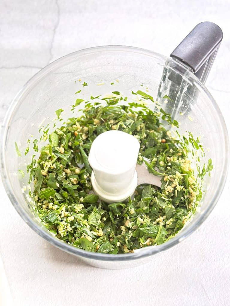 The ingredients—grated Parmesan, toasted pine nuts, garlic, and basil—are placed in a food processor and pulsed to achieve a coarse texture.