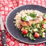 Sliced crispy chicken served over a bed of brown rice, accompanied by a zucchini and cherry tomato salad, topped with a dollop of sour cream and garnished with fresh coriander leaves.