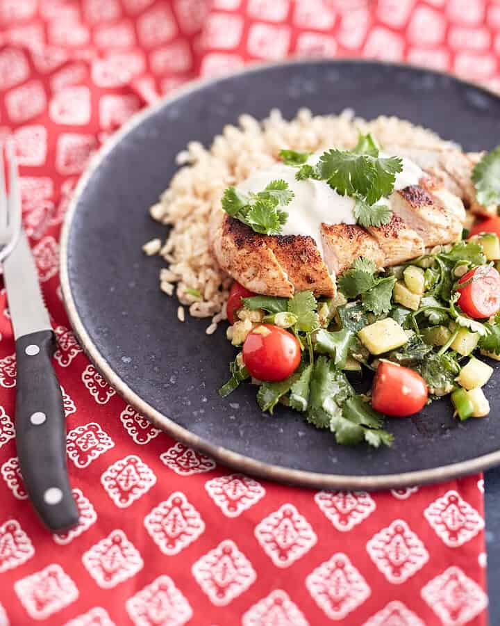 Sliced crispy chicken served over a bed of brown rice, accompanied by a zucchini and cherry tomato salad, topped with a dollop of sour cream and garnished with fresh coriander leaves.