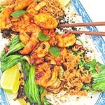 A plate of tiger prawns and bok choy on a bed of jasmine rice, topped with crispy chili onion and black sesame seeds, served with a lime wedge on the side.