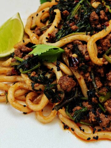 Beef udon noodles in a glossy sauce topped with coriander, chilli, sesame seeds and lime wedge.