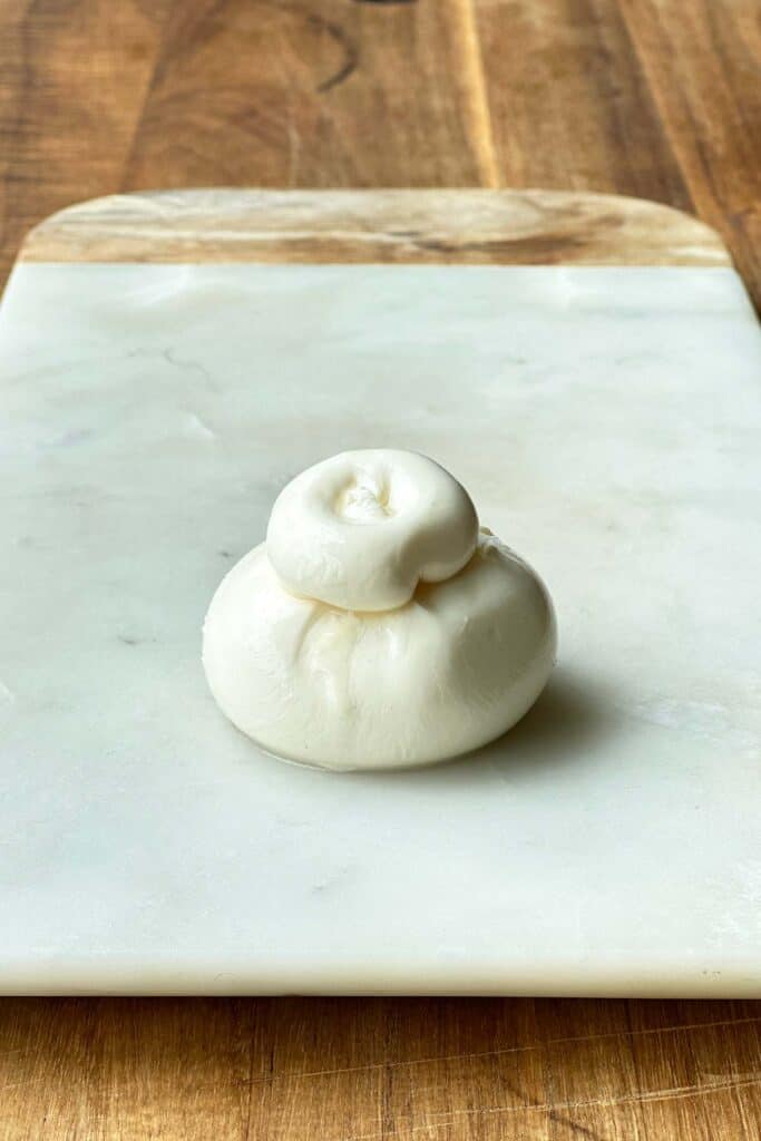 A ball of burrata cheese sits on a marble cheese board.