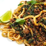 Beef udon noodles in a thick, flavourful sauce topped with fresh coriander, specks of chili, black sesame seeds, and a lime wedge on the side, on a white plate.